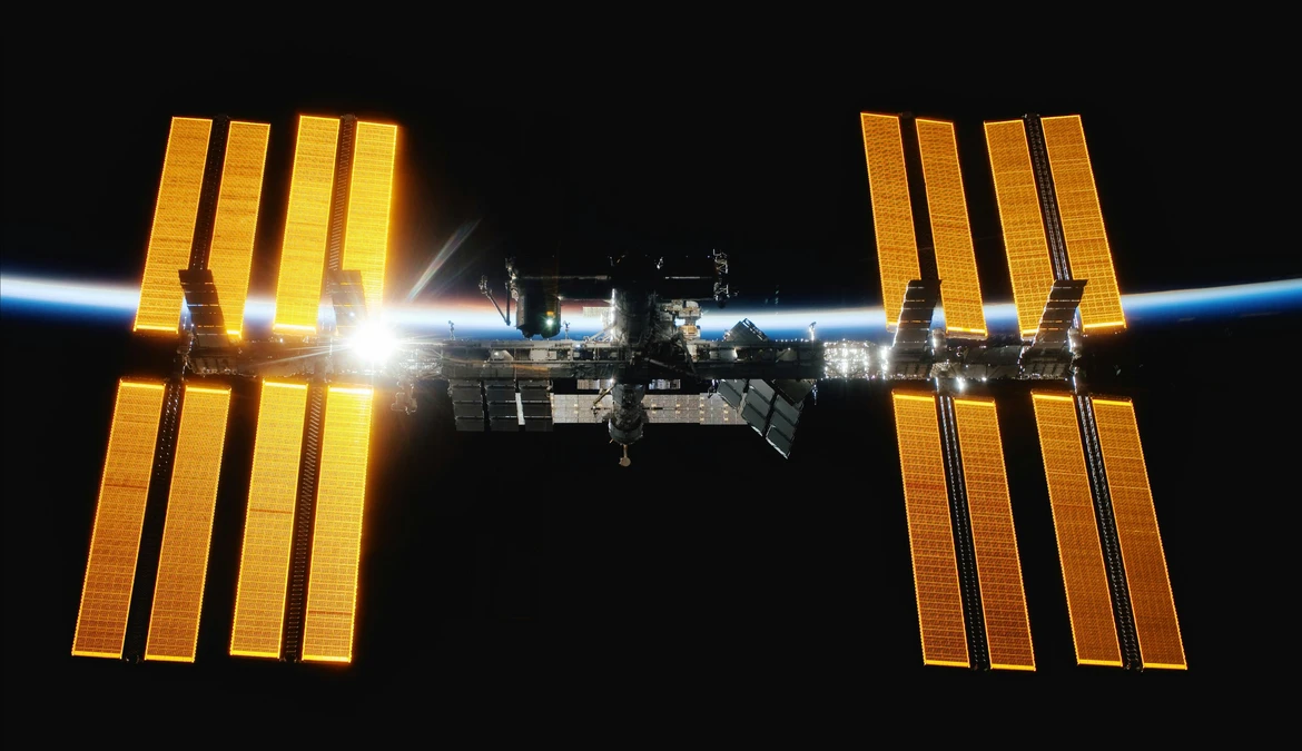 The International Space Station in orbit, its solar arrays lit gold against the curve of the Earth