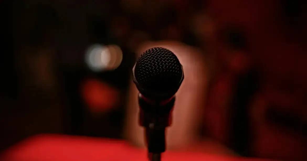 A close-up of a microphone against a dark, blurred background with a red hue.
